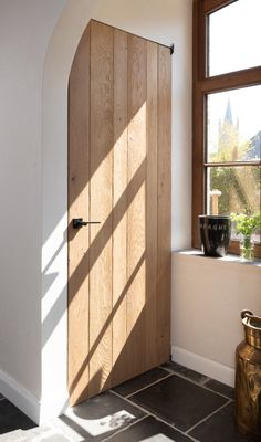 an open wooden door in front of a window with potted plants on the floor