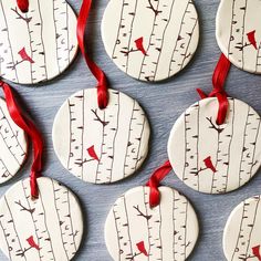 six ceramic ornaments with red ribbon hanging from the tree's bark and birds painted on them