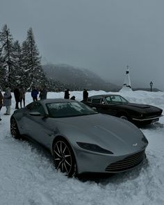 two cars are parked in the snow with people standing around them and one is black