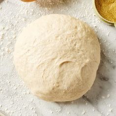 a ball of dough sitting on top of a table next to some flour and measuring spoons