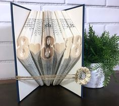 an open book with folded pages is sitting on a table next to a potted plant