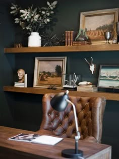 a desk with a lamp and some pictures on the shelf above it in a room that has dark green walls