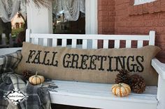 a pillow that says fall greetings sitting on a bench next to some pumpkins