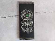 a black plaque with a green stone in the center on a white wall next to a plant