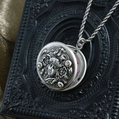 "Locket: Created from original Art Nouveau metal dies circa 1905. Beautiful stylized image is embossed in relief, and accented with three crystals. Fits two photos. Chain: Slinky high quality double rope Hand burnished silver Locket: 1-1/4\" Chain: 17\" Created and produced in our Los Angeles studio" Ornate Medallion Jewelry, Ornate Medallion Stamped Jewelry, Ornate Engraved Locket Necklace For Keepsake, Ornate Engraved Locket Necklace Vintage Collection, Victorian Antique Silver Stamped Jewelry, Antique Silver Stamped Victorian Jewelry, Victorian Style Stamped Antique Silver Jewelry, Vintage Silver Locket Necklace With Intricate Design, Ornate Engraved Antique Silver Locket Necklace