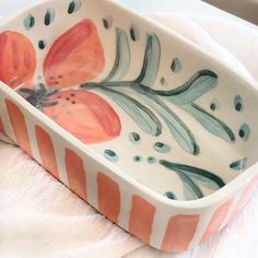 an orange and white flowered ceramic dish on a tablecloth with pink flowers in the background