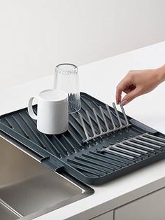 a person holding a knife and fork over a sink with a cup on the tray