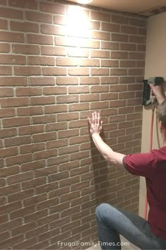 a man is sitting on a chair in front of a brick wall with his hands up