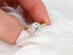 a person's hand holding a ring with a diamond on it and white feathers in the background