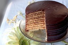 a chocolate cake with one slice cut out on a plate next to flowers and leaves