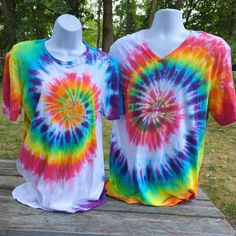 two t - shirts are sitting on a wooden table in front of some trees and grass