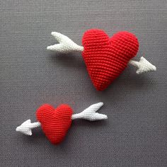 two knitted hearts and an arrow on a gray surface with white arrows pointing towards each other