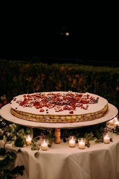 a cake sitting on top of a white table covered in candles and greenery next to a hedge