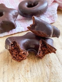 three chocolate donuts with one broken in half on a wooden table next to pink napkins