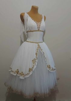 a white dress with gold trimmings on the waist and shoulder, sitting on a mannequin