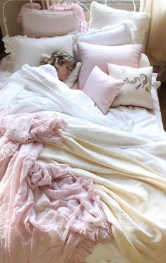 a white bed topped with lots of pillows next to a night stand filled with blankets