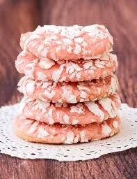 a stack of pink and white cookies on a doily next to a wooden table