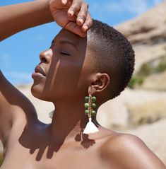 a woman with no shirt on holding her hair up to her head and wearing earrings