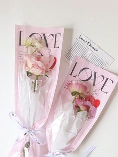 three pink roses wrapped in cellophane and tied with ribbon on top of a magazine