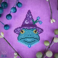 a cross - stitch pattern with an image of a green frog wearing a purple hat