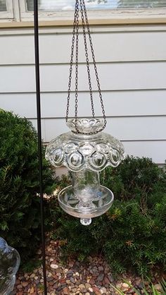 a glass bird feeder hanging from a chain in front of a house with moss growing around it