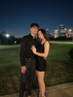 a man and woman standing next to each other in front of a field at night