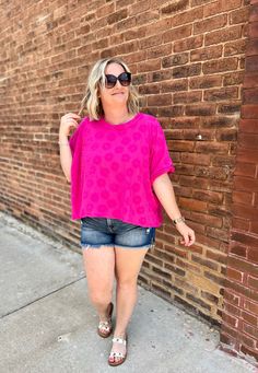 a woman standing in front of a brick wall with her hands on her hips and wearing sunglasses