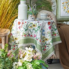 a table with flowers and vases on it in front of a chair next to a potted plant