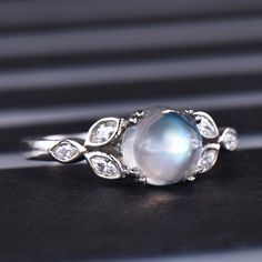 a ring with a large white pearl surrounded by diamonds on a black surface, in front of a window