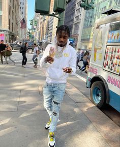 a young man is walking down the street while looking at his cell phone and eating ice cream