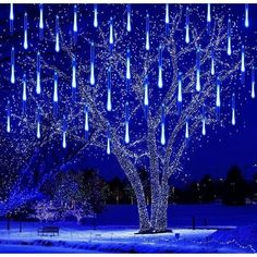 a lighted tree in the middle of a snowy field with blue lights hanging from it's branches