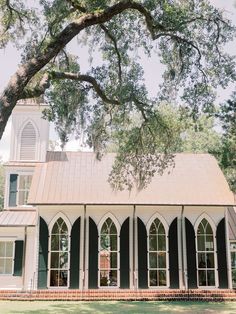 an old church with green shutters and a clock tower in the background under a large oak tree