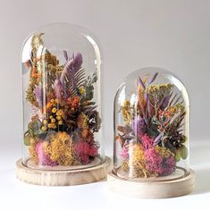 two glass domes filled with plants and flowers on top of wooden bases, sitting on a white surface