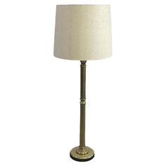 a lamp with a white shade on top of it and a gold metal pole base