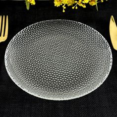 a glass plate sitting on top of a table next to silverware and yellow flowers