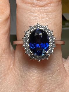 a woman's hand with a blue ring on top of her finger and an oval shaped diamond in the middle