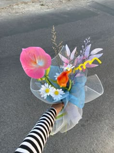 a person holding a bouquet of flowers on the side of the road in their hand