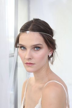 a woman with blue eyes wearing a white dress and headband in front of a window