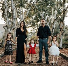 a man and two girls holding hands while standing in front of trees