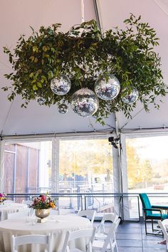 an indoor tent with tables and chairs, hanging from the ceiling filled with disco ball decorations