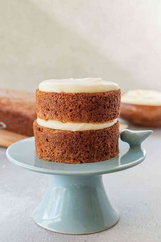 a three layer cake with white frosting on a blue plate next to a loaf of bread