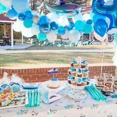 a table topped with blue and white balloons next to a brick wall covered in food