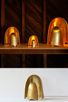 three golden bell shaped objects sitting on top of a wooden shelf next to each other