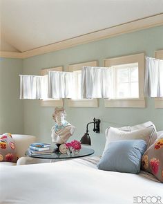 a white bed with pillows on top of it and two windows in the back ground