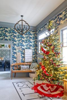 a decorated christmas tree in the corner of a room with blue and white wallpaper