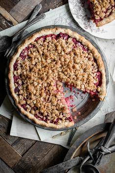 a pie with crumbled toppings is on a table next to two plates and utensils