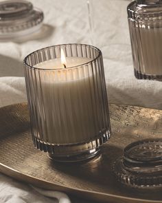 a lit candle sitting on top of a metal tray next to two glass containers with lids