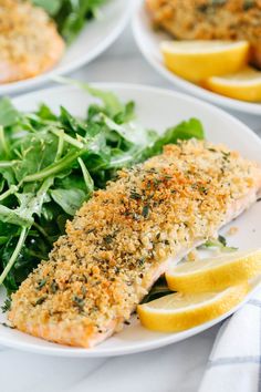 two white plates topped with fish next to lemon wedges and spinach leaves on a table