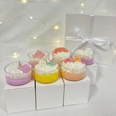 four desserts in small glass bowls on top of white boxes with lights behind them