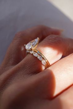 a woman's hand holding a gold ring with two pear shaped diamonds on it